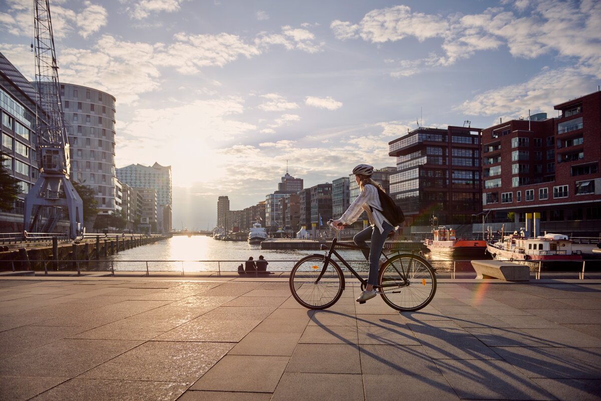 Egy bicikliző nő egy folyó partján, a városban.
