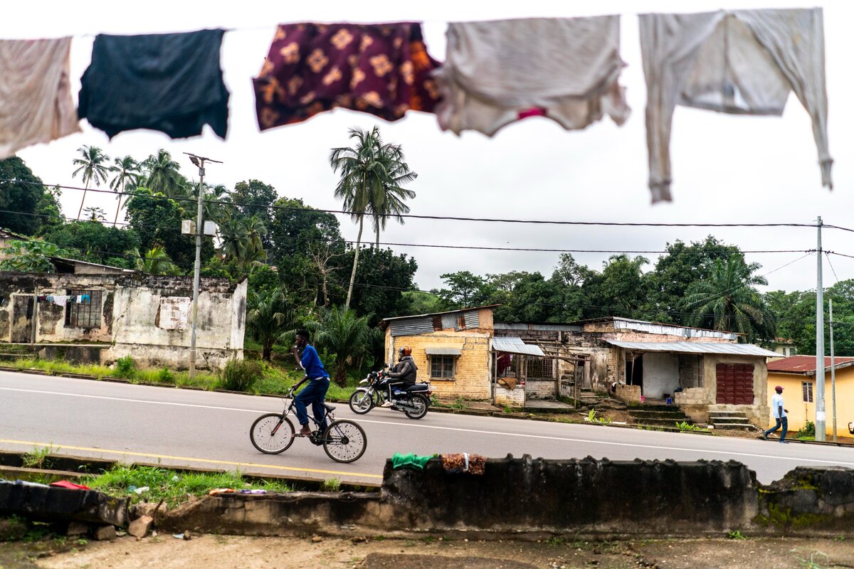 Motorkerékpárok és kerékpárok osztoznak az úton a forgalmas Kono utcáin Konóban, Sierra Leonéban 2021. október 8-án, pénteken. Susan Lebbies édesanyja meghalt a szülés közben. Sierra Leonéban a legmagasabb az anyai halálozási arány a világon. Lebby a nagymamája halála óta, aki felnevelte, tizenéves kora óta otthonról otthonra ugrált. Most terhes, és másoktól függ, hogy szállást kapjon, és eltökélt szándéka, hogy nem hal meg szülés közben, mint az édesanyja. Kapcsolatba lépett egy jóindulatú bábával, Aminata Saiduval, egy hagyományos szüléssegítővel, és most a Partners in Health Wellbody klinikán kap támogatást és ellátást. Még ha Susan normális szülésen is megy keresztül, akkor is a nagybátyjától függ a lakhatása, egy gyermeket kell eltartania, nem fejezte be az iskolát, és nem dolgozik. Susan jövője bizonytalan.