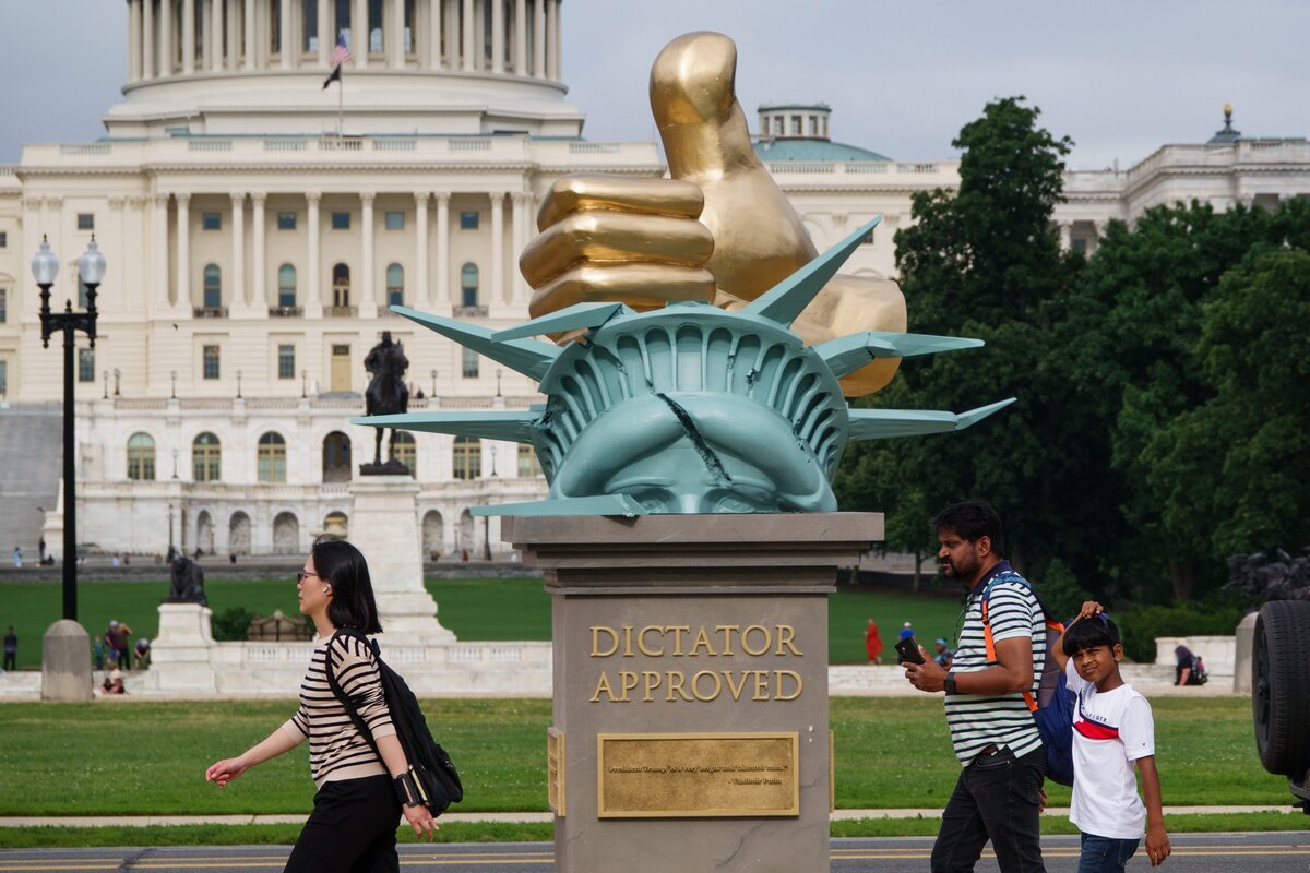 A Donald Trump amerikai elnöknek címzett, „Dictator Approved” (Diktátor jóváhagyta) című szobor a National Mallban, az amerikai Capitolium épületével a háttérben, 2025. június 17-én, Washingtonban. A szobor egy összetört Szabadság-szobor tetején arany hüvelykujjal látható, valamint különböző diktátorok Trumpot támogató idézetei is olvashatók rajta.